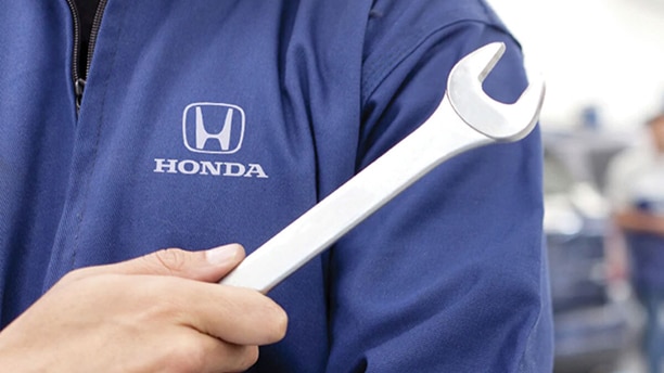 A close-up of a Honda technician holding a wrench. The technician has a Honda logo on their shirt in focus in the image.